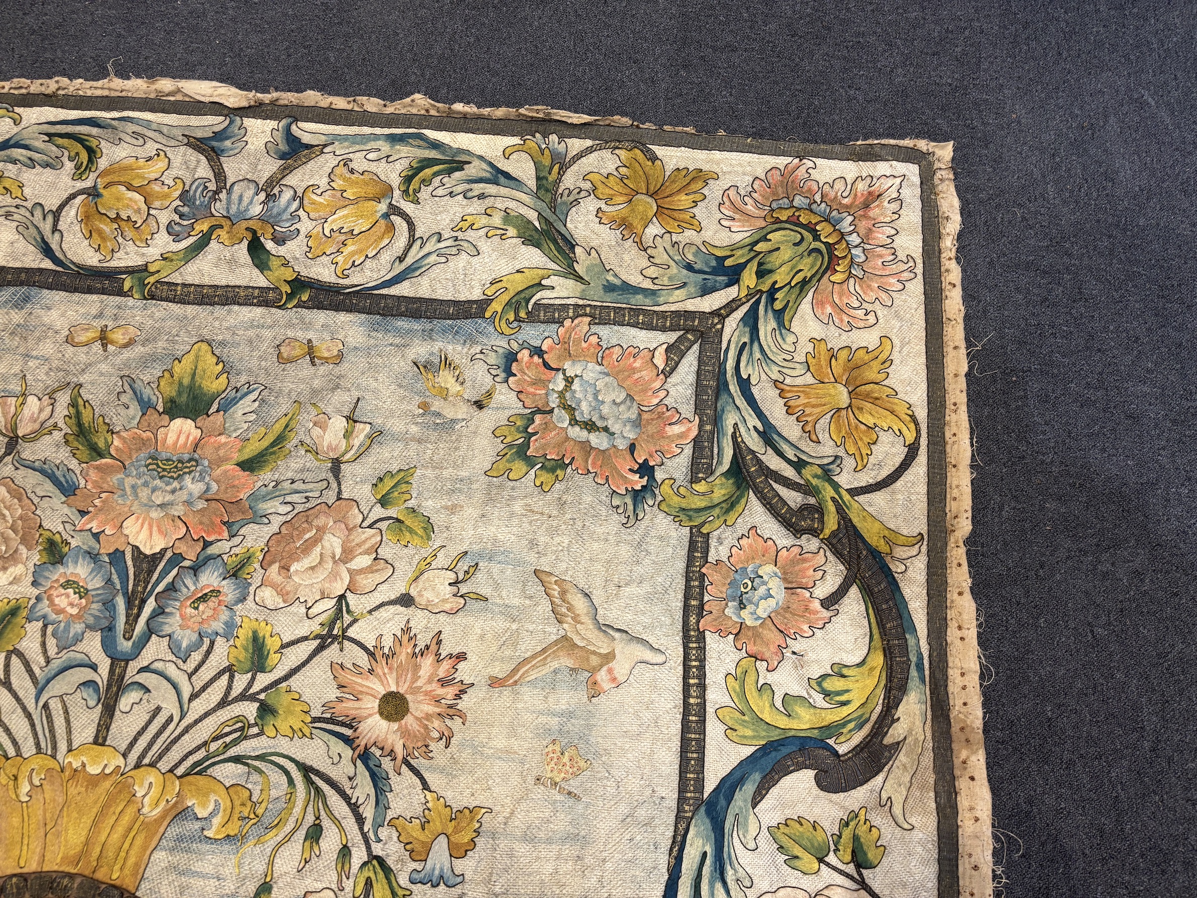 A large early 18th century possibly French polychrome and gold metallic silk embroidered wall hanging, with scrolling vine and floral border. The central motifs embroidered with an elaborate metallic thread cartouche fra